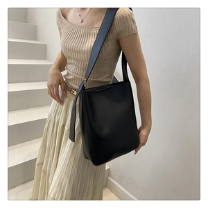 Minimalist black bucket bag shown with wide shoulder strap on model in minimalist setting