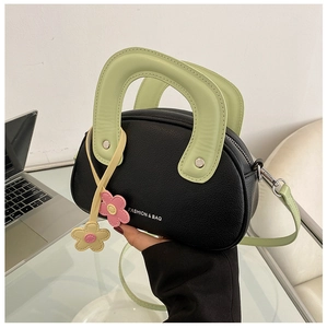 Détail du sac à main noir et vert avec des charms floraux et une fermeture éclair en métal