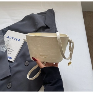 Détail du sac seau crème à motif crocodile avec breloque dorée et bandoulière