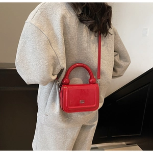Détail du sac à main rouge en cuir verni brillant avec logo en métal et poignées