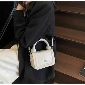 Détail du sac à main crème avec poignée sphérique et logo métallique sur un escalier