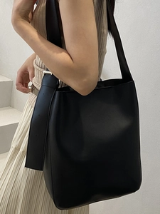 Minimalist black leather bucket bag with wide strap and golden buckle on model