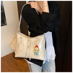 Close-up of cream soft leather tote bag with cartoon doll pendant worn by a model