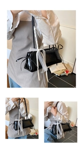 Détail du sac à bandoulière noir brillant avec rubans de dentelle et nœud blanc
