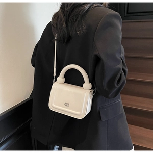 Détail d'un mini sac carré beige crème avec poignée cylindrique et logo métallique
