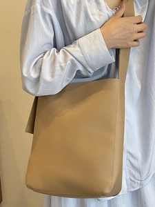 Minimalist khaki leather bucket bag with top stitching shown on model's shoulder