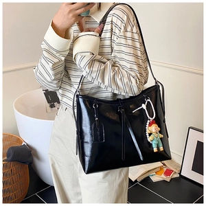 Detail shot of black glossy patent leather tote bag with cute doll charm and pearl chain