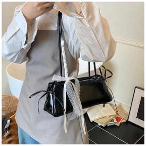 Détail d'un sac à bandoulière en cuir verni noir avec un nœud décoratif en dentelle blanche