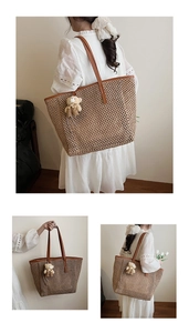 Detail of a large straw tote bag featuring brown leather straps and a cute teddy bear charm