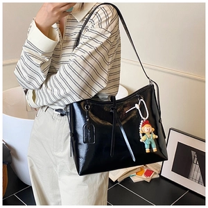 Detail view of glossy black tote bag with long straps and a cute cartoon charm