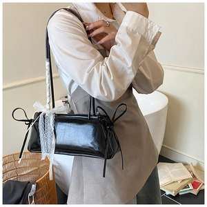 Détail du sac bandoulière noir brillant avec nœud en dentelle blanche et attaches de côté