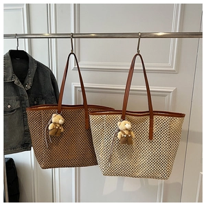 Detail of hollow woven straw tote bag featuring brown leather straps and plush bear charm