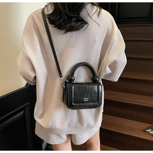 Détail d'un sac à main chic en cuir verni noir avec logo argenté et poignée élégante
