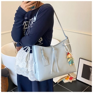 Light blue glossy tote bag with pearl chain and doll pendant shown in a crossbody style