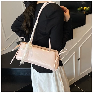 Sac bandoulière rose en cuir verni avec dentelle blanche et nœud, porté par un mannequin