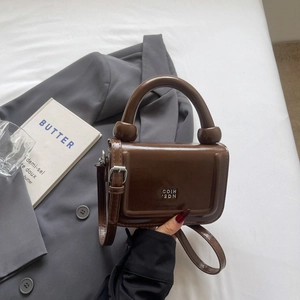 Détail d'un sac à main carré marron brillant avec logo métallique et poignée anneau