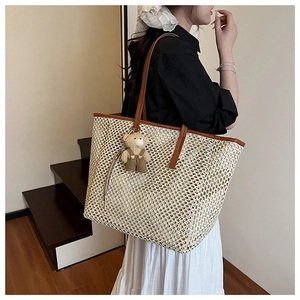 Macro detail of straw woven tote with leather trim and a cute teddy bear charm