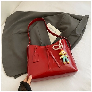 Detailed macro view of glossy red leather tote bag with a charming cartoon doll pearl pendant
