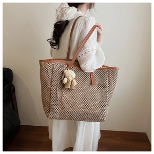 Close-up of beige woven straw tote bag with brown handles and a cute bear pendant