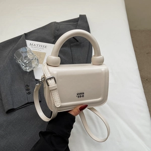 Détail du mini sac carré blanc crème avec poignée cylindrique et emblème doré