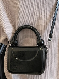Sac bandoulière minimaliste en cuir verni noir avec poignée emblématique à double boule