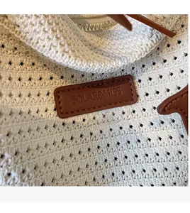 Detail of hollow woven texture and brown leather logo tag on beige straw tote bag
