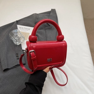 Détail du sac carré en cuir verni rouge avec poignée ronde et logo en métal