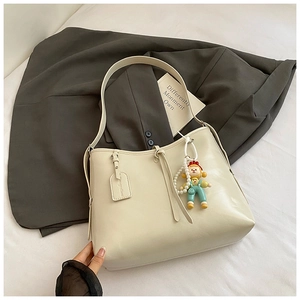 Detail of soft cream white shoulder bag with pearl chain doll pendant on white bedding