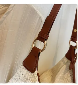 Close-up of golden metal ring hardware on a cream woven straw tote bag shoulder strap