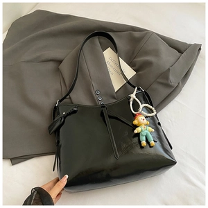 Close-up of black glossy leather tote bag with a cute cartoon doll charm and leather tag