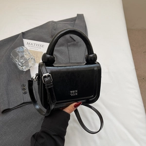 Détail du sac minimaliste en cuir noir avec poignée ronde unique et lettrage argenté brillant