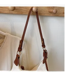 Detail of adjustable brown leather shoulder strap with gold metal ring on woven tote bag