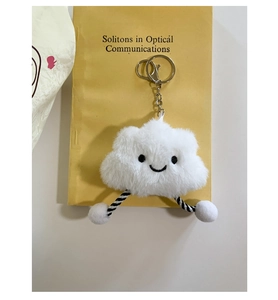 Detail of a white plush cloud charm with embroidery and spiral legs on a book