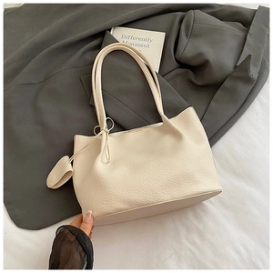 Detail of cream tote bag with lychee texture and knot detail on a grey suit