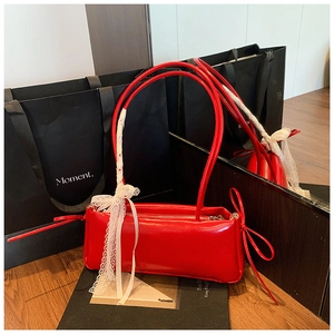 Détail du sac à bandoulière rouge brillant avec nœuds en cuir et ruban en dentelle