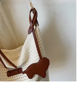 Macro detail of cream woven tote with brown leather strap and puppy charm decoration