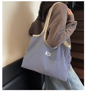 Detail of navy blue striped canvas tote bag with beige leather handles and logo tag