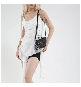 Sac bandoulière noir chic avec chaîne argentée et boucle ronde sur robe blanche