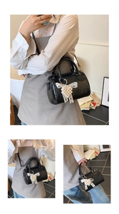 Detail of black patent leather Boston bag with pearl bow charm and detachable strap
