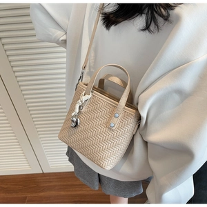 Detail der beigen geflochtenen Beuteltasche mit Herzanhänger und verstellbarem Schultergurt