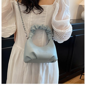 Close-up of light blue grain leather handbag with ruched handle and metal chain detail