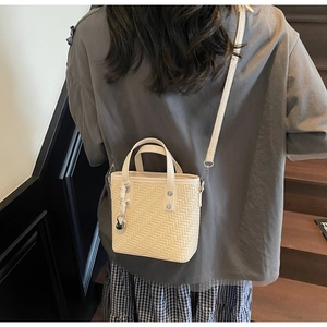 Detail der cremefarbenen gewebten Mini-Tasche mit Herzanhänger auf einer Holztreppe
