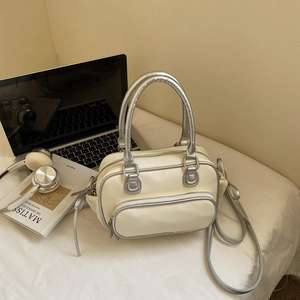 Minimalist beige bowling bag styled with silver handles on a white fabric surface