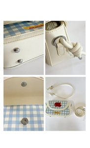 Detail view of plaid flap handbag featuring apple embroidery and magnetic closure mechanism
