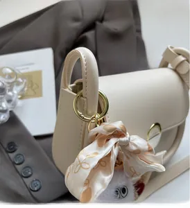 Détail du sac selle crème avec anneau doré et foulard en soie sur la poignée
