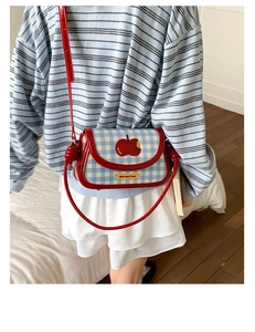 Close-up of red patent leather crossbody bag with blue plaid flap and apple embroidery