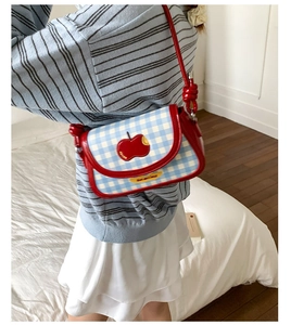 Detail of blue and white checkered crossbody bag with red apple patch and gold logo plaque