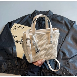 Detailansicht beige geflochtene Beuteltasche mit silbernem Anhänger und Lederriemen