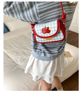Detail of a red shiny saddle bag with blue-white plaid flap and apple patch embroidery