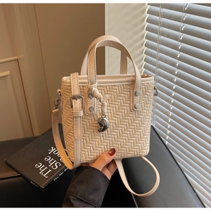 Detail der cremefarbenen geflochtenen Tasche mit Herzanhänger und verstellbarem Gurt